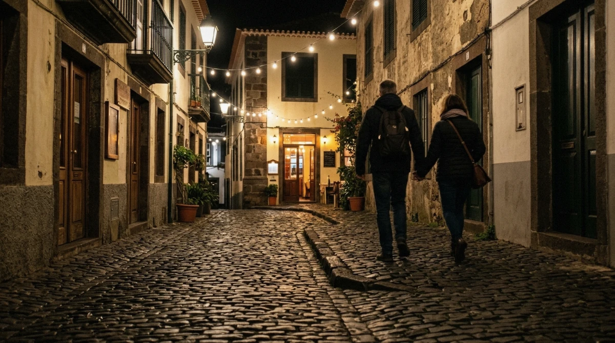 A lamplit lane in Funchal, Portugal at night with a couple walking toward a lit doorway