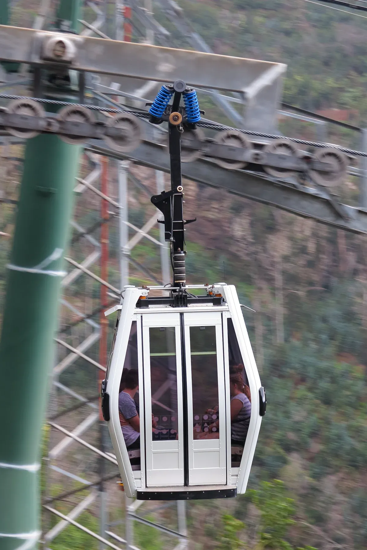 A Funchal cable car cabin with visible passengers passing a support tower on the ride to Monte, Funchal, Madeira