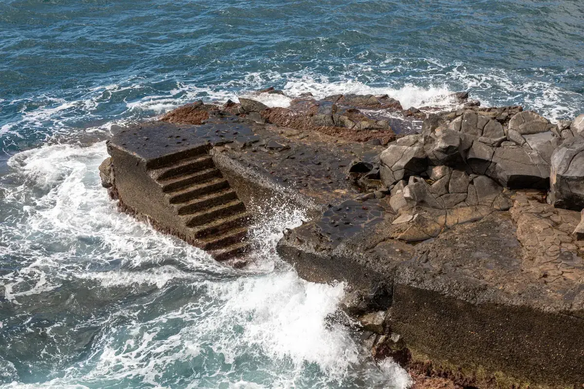 Concrete steps and volcanic rock leading into a stormy Atlantic near the Lido bathing area in Funchal, Madeira