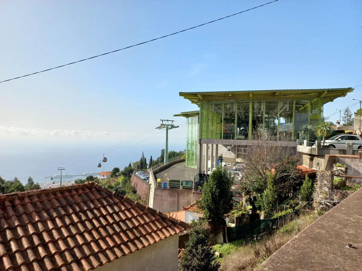 The green glass upper station of the Funchal cable car at Largo das Babosas in Monte, Madeira, with a cabin descending toward the harbour