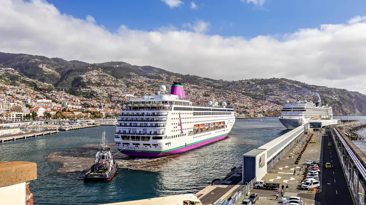 A cruise ship being guided into the Funchal cruise port with the city and hills behind, Madeira, Portugal