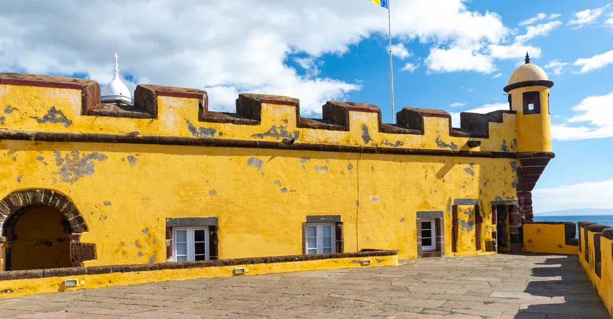 The yellow ochre walls, whitewashed chapel dome and corner turret inside the Sao Tiago fort courtyard in Funchal, Madeira